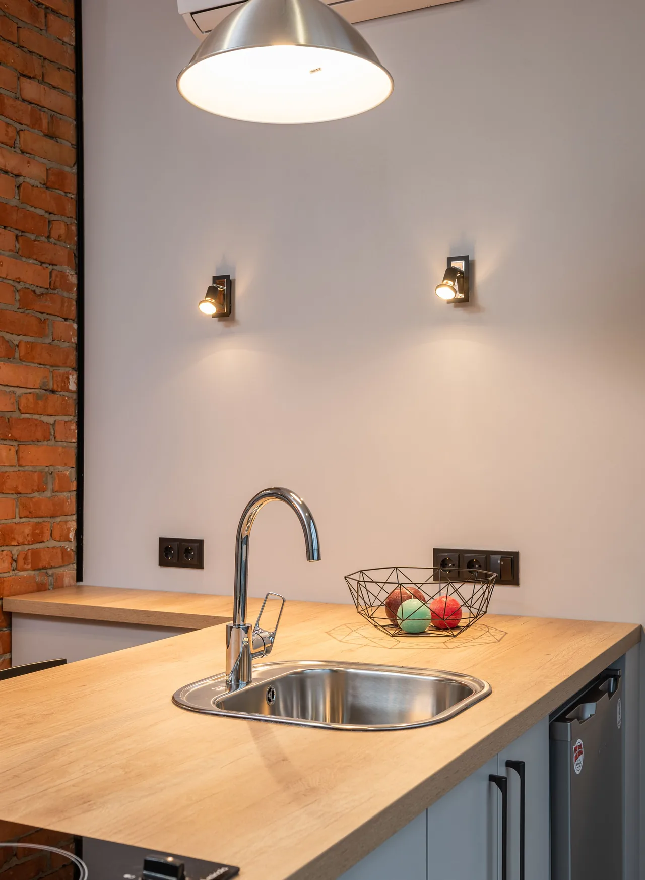 Wooden kitchen counter with a stainless-steel sink, gray cabinets and a wire fruit basket.